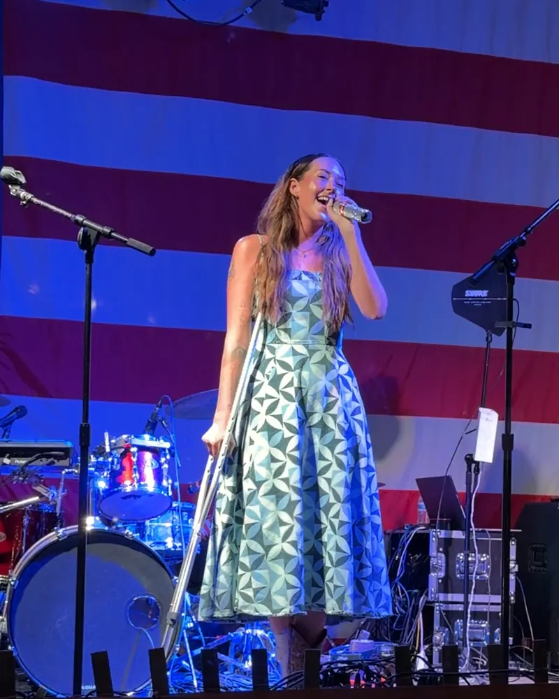 Bella Popa singing in front of an American flag backdrop on an outdoor stage