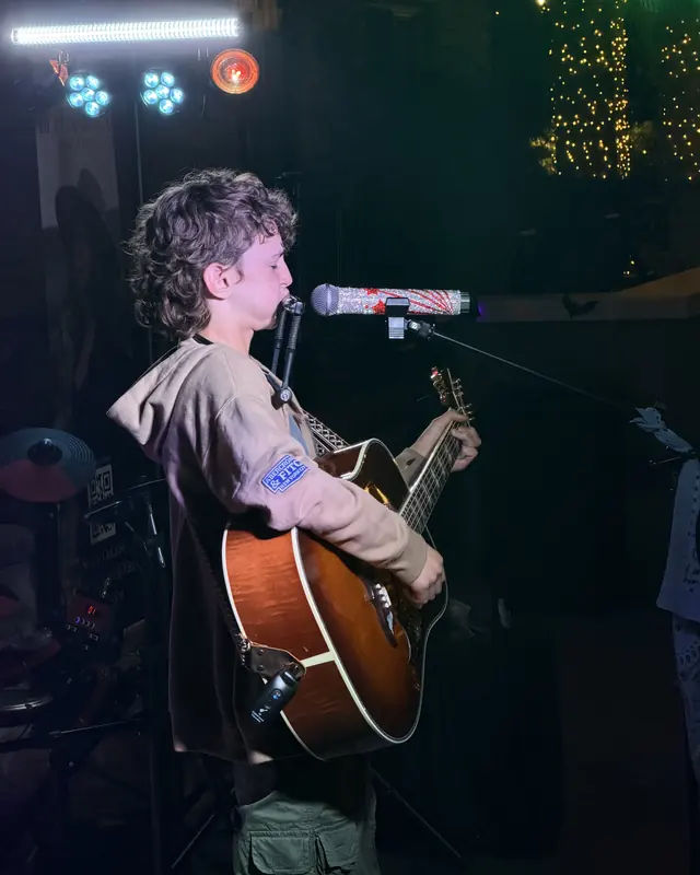 Young guitarist singing under the stage lights at the open mic